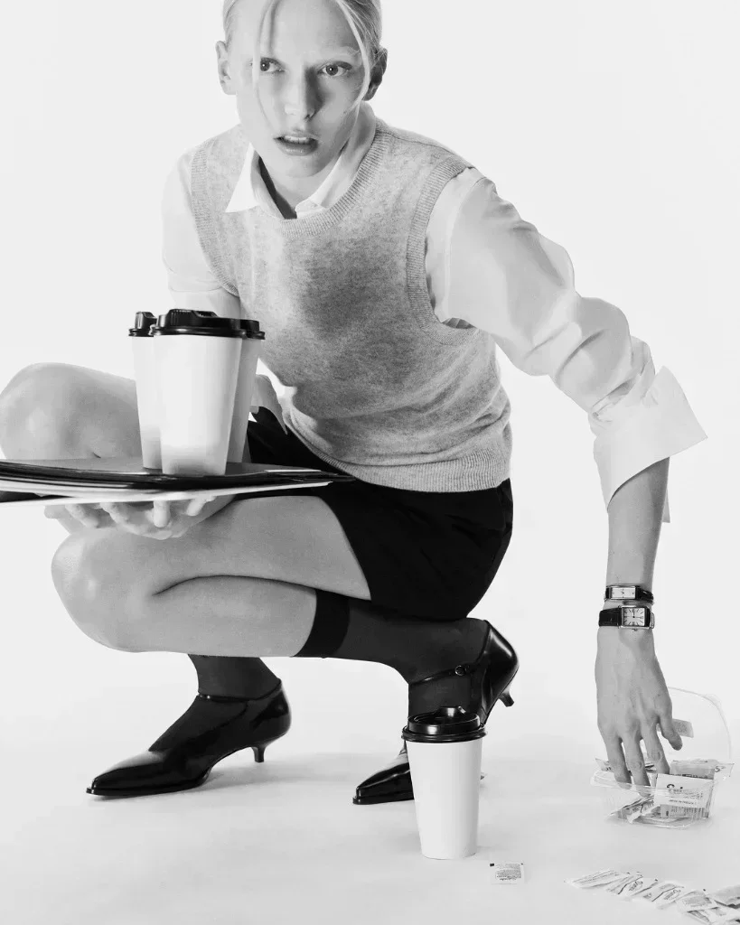 Alex Consani as The Junior Associate balancing a coffee run