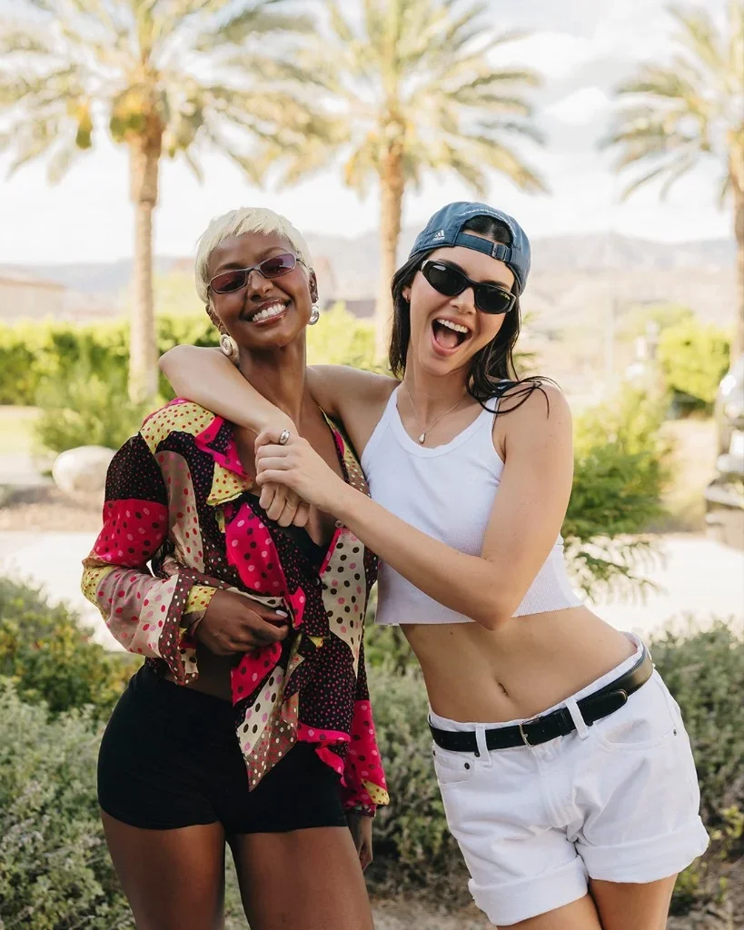 Candid portrait of Kendall Jenner laughing at the 818 Outpost in her reversed Adidas cap, Éterne cropped tank, and Levi's 501 shorts