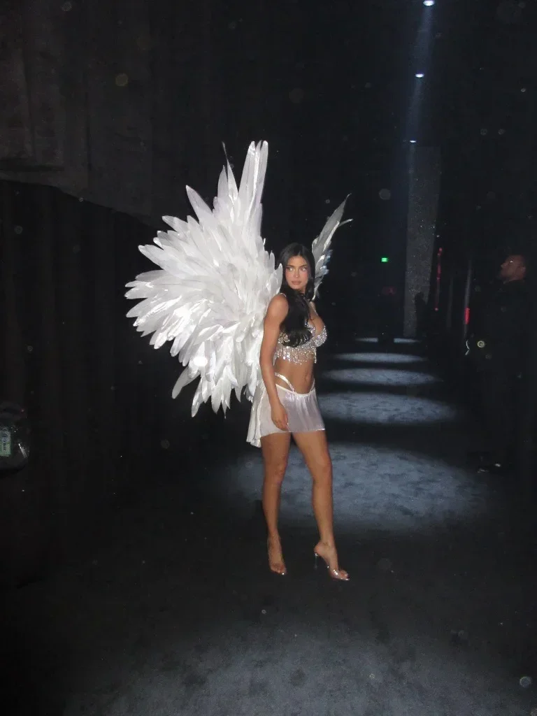 Kylie Jenner in the backstage corridor framed by white Angel wings
