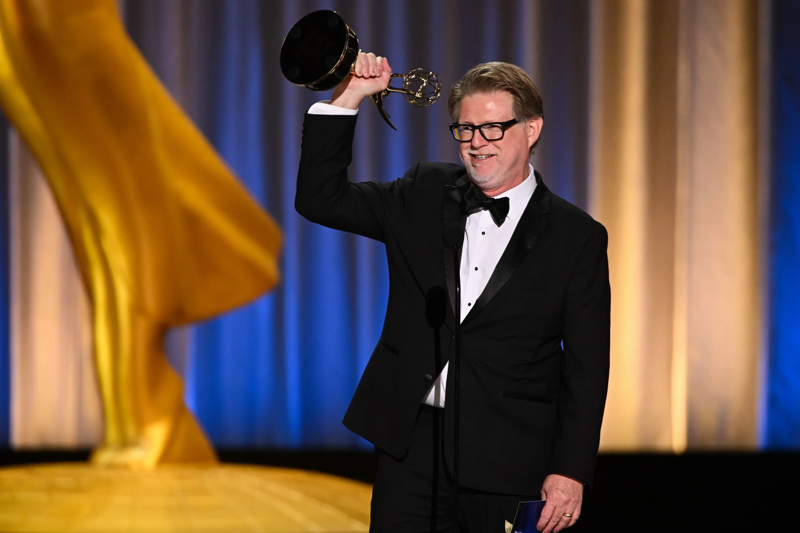 Series creator raising Emmy statuette in triumphant celebration on stage