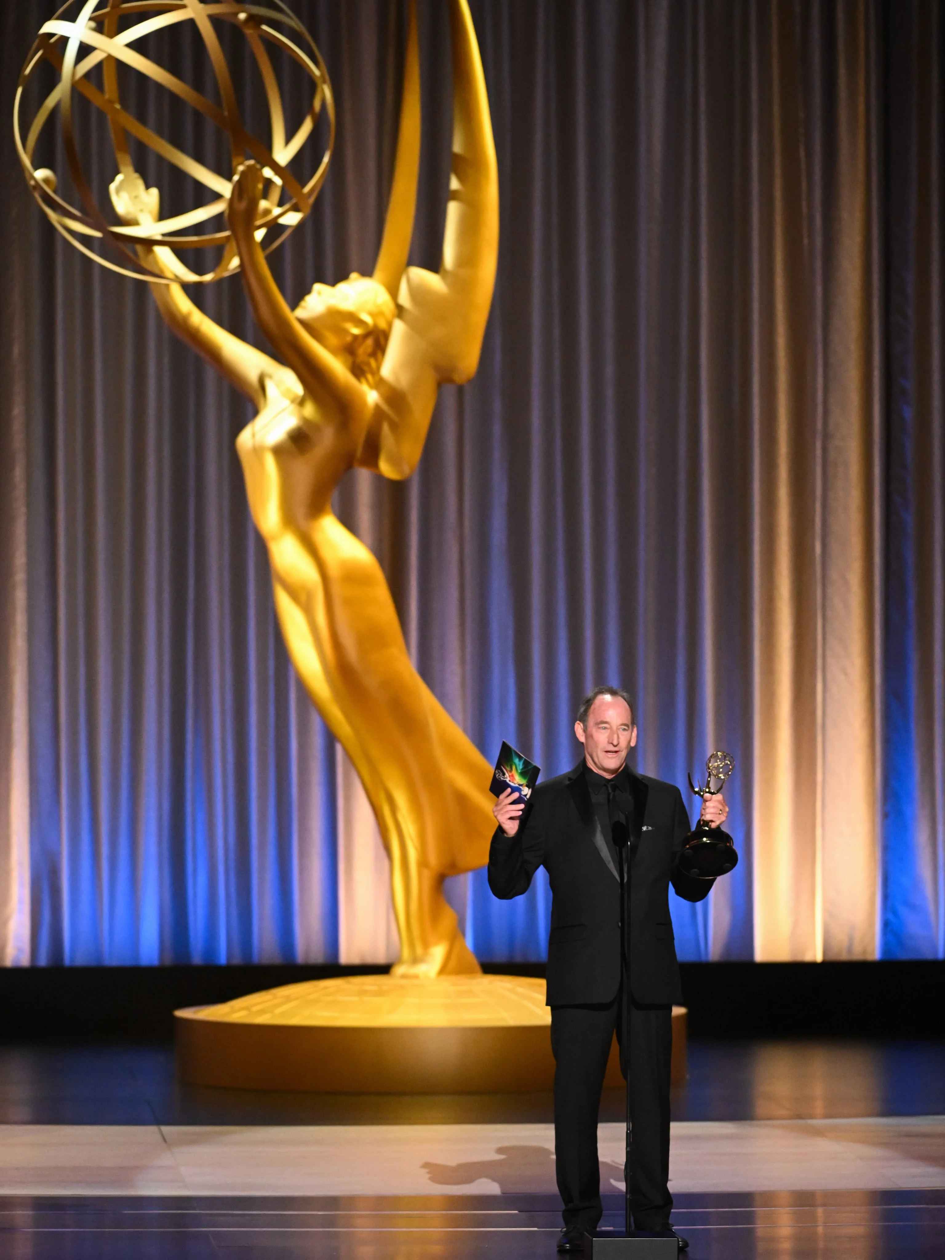 Jessica Gunning wiping tears of joy at the microphone holding her Emmy