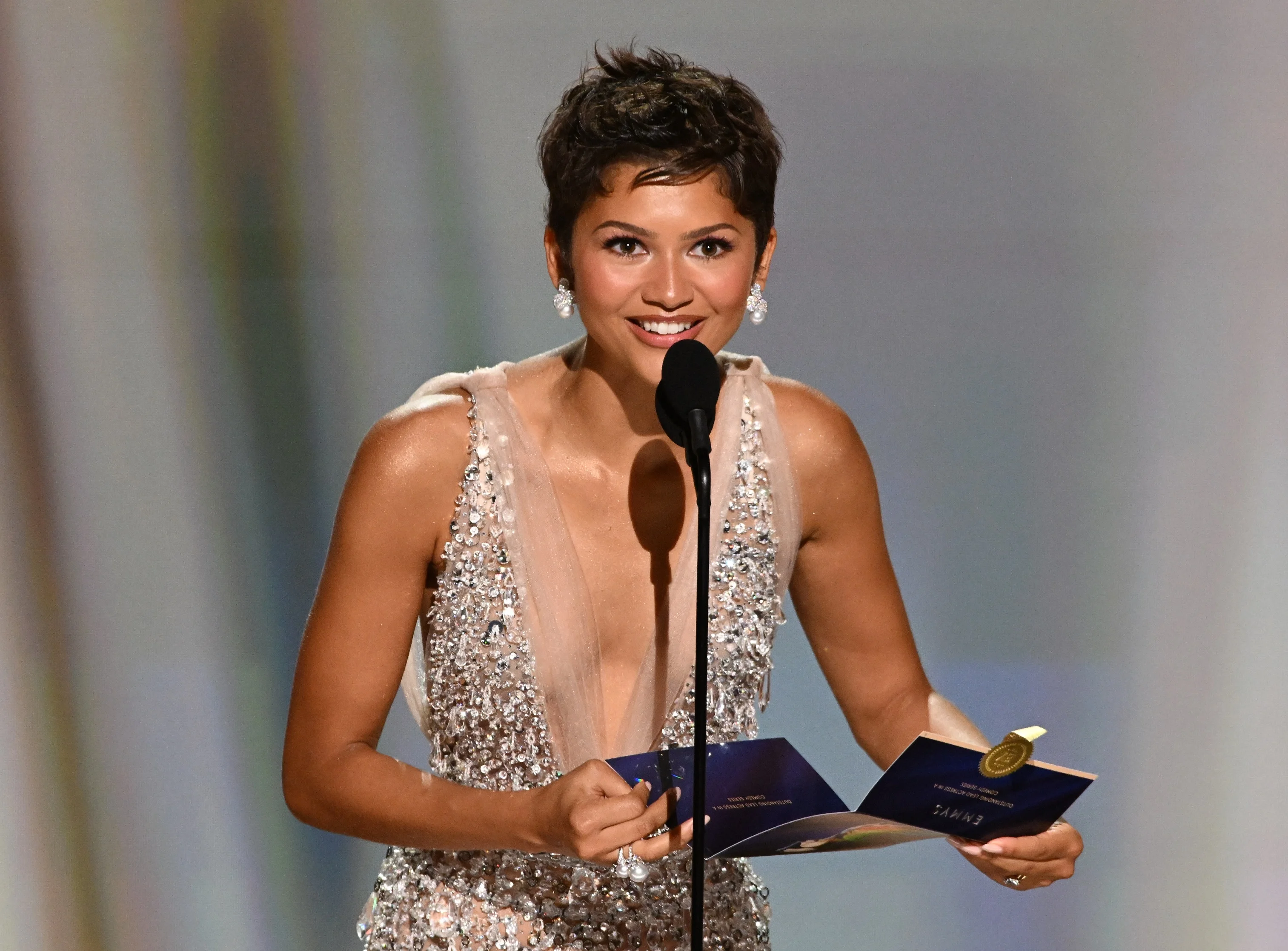 Zendaya speaking into the podium microphone with a radiant smile