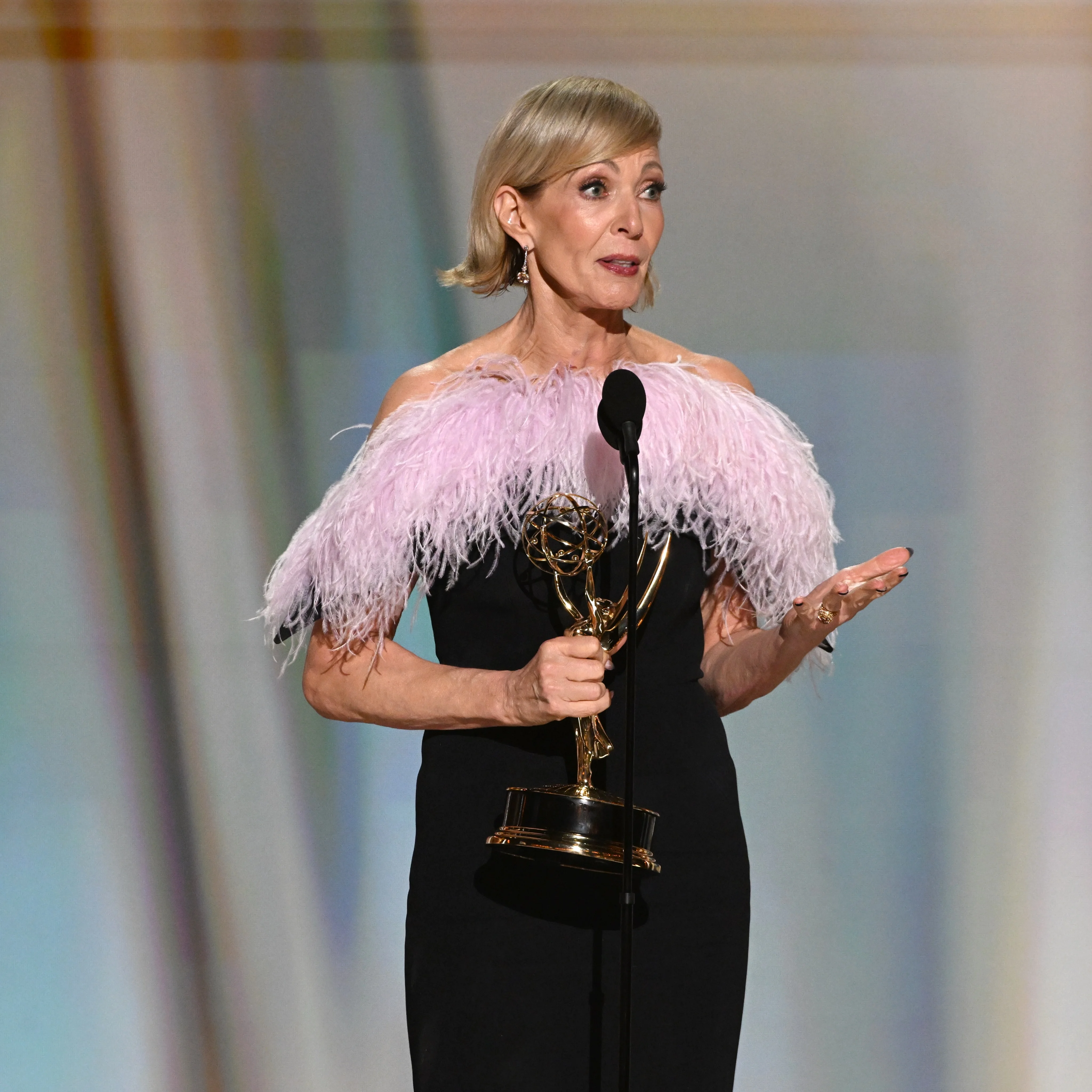Jane Lynch holding Emmy wearing black gown with lilac ostrich feather trim