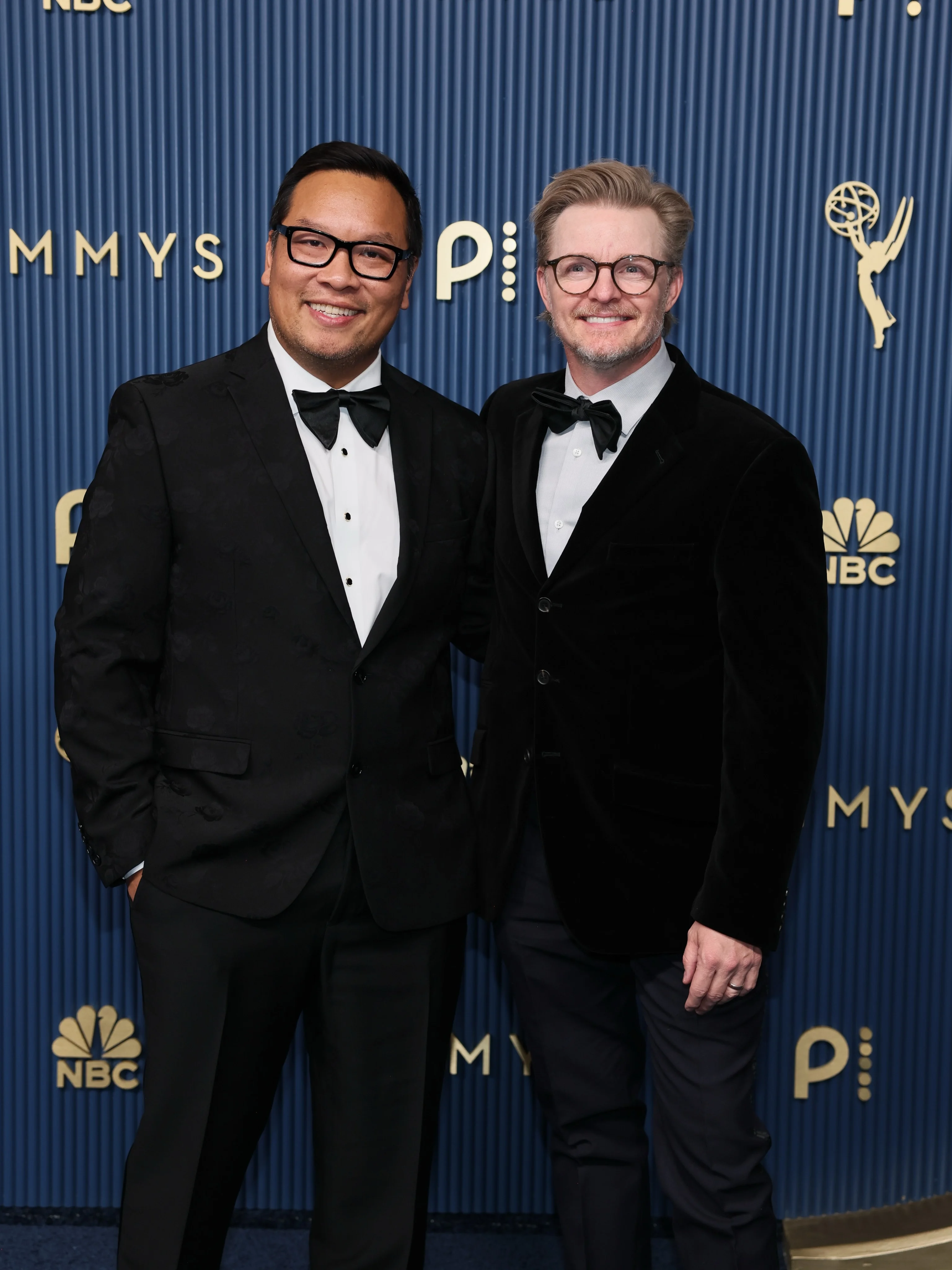 Two creative partners in classic eveningwear smiling against the blue Emmy backdrop