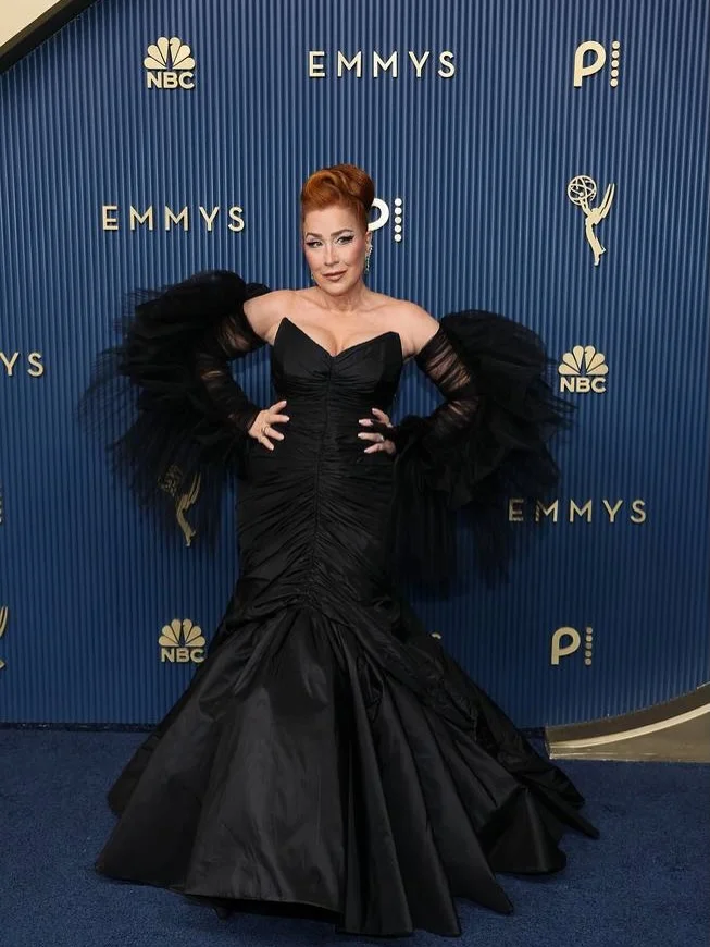 Rebecca Romijn posing in black evening gown with dramatic feathered sleeves