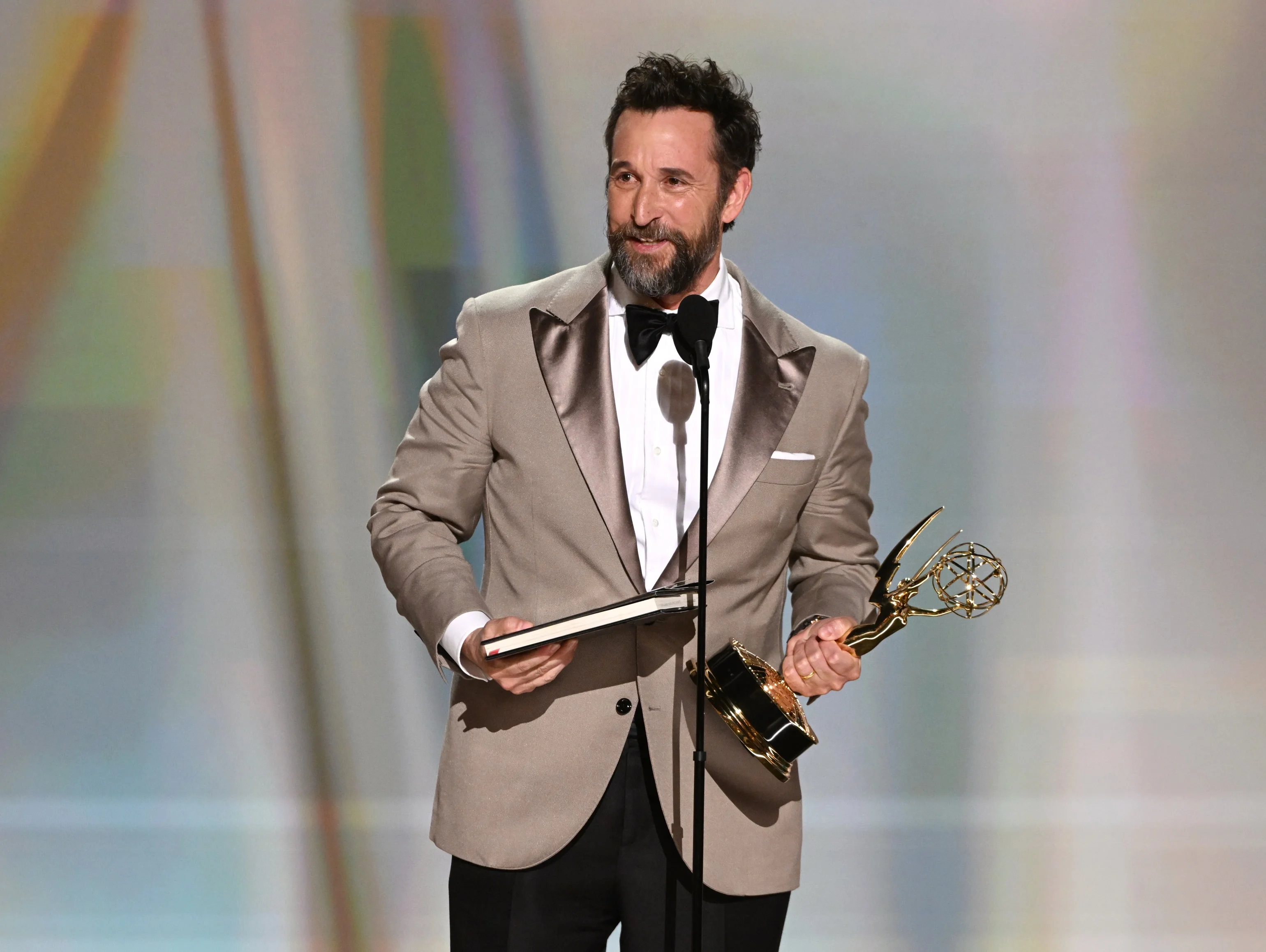 Winner in elegant taupe dinner jacket holding Emmy and acceptance envelope
