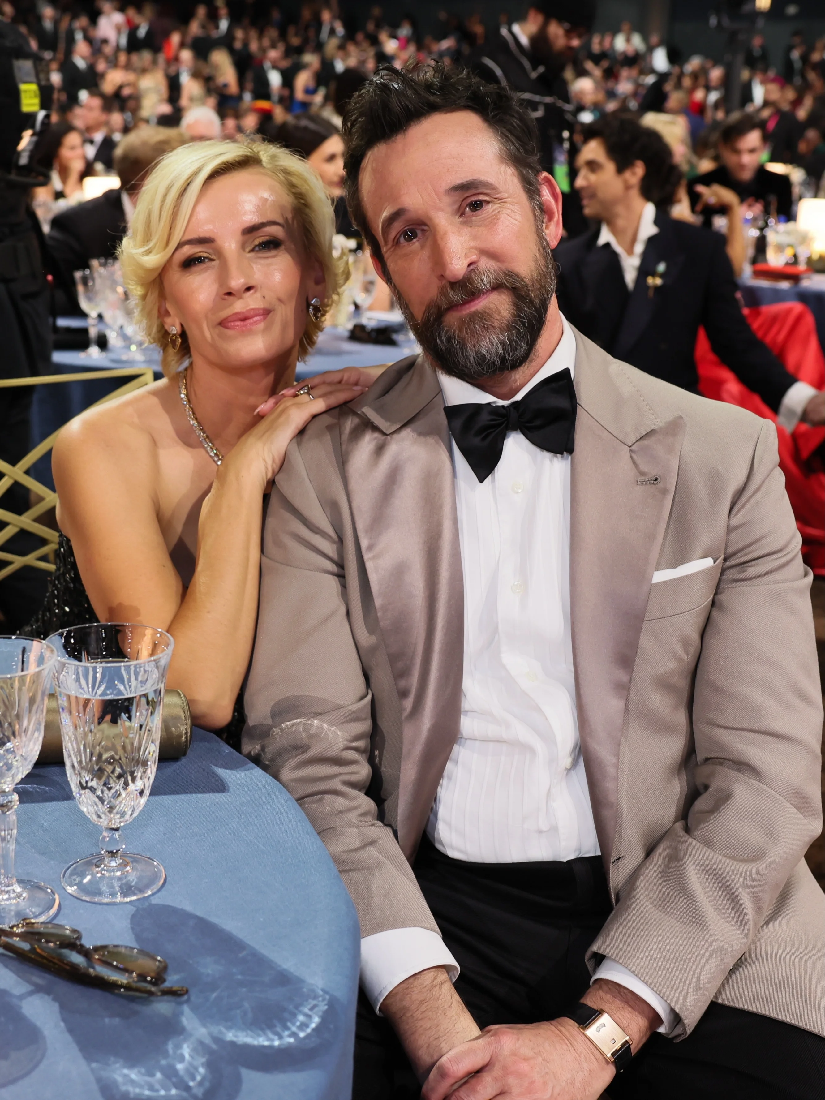 Noah Wyle and Sara Wells sharing an intimate smile at their ballroom table