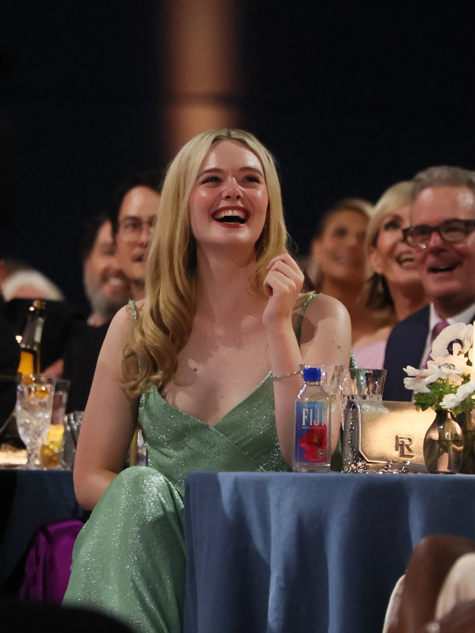 Elle Fanning laughing spontaneously at table in seafoam green sequin gown