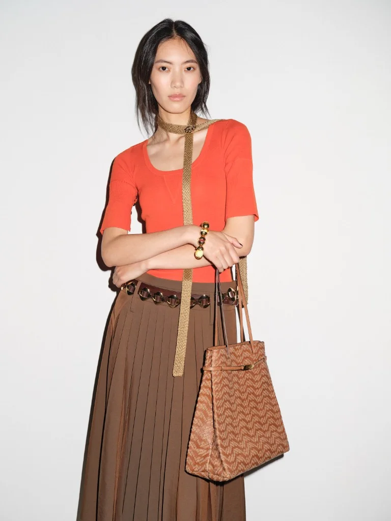 Tory Burch Spring 2027 persimmon knit top, pleated skirt, double-wrap belt, and patterned tote