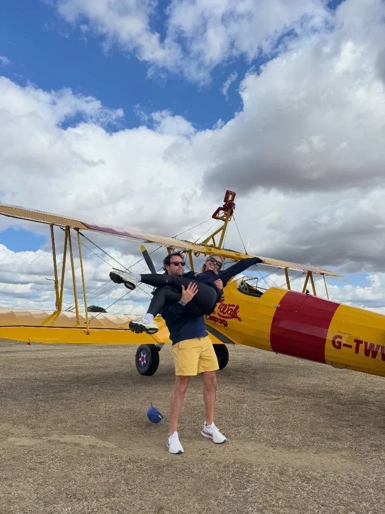 Scooter Braun carrying Sydney Sweeney in front of a yellow biplane